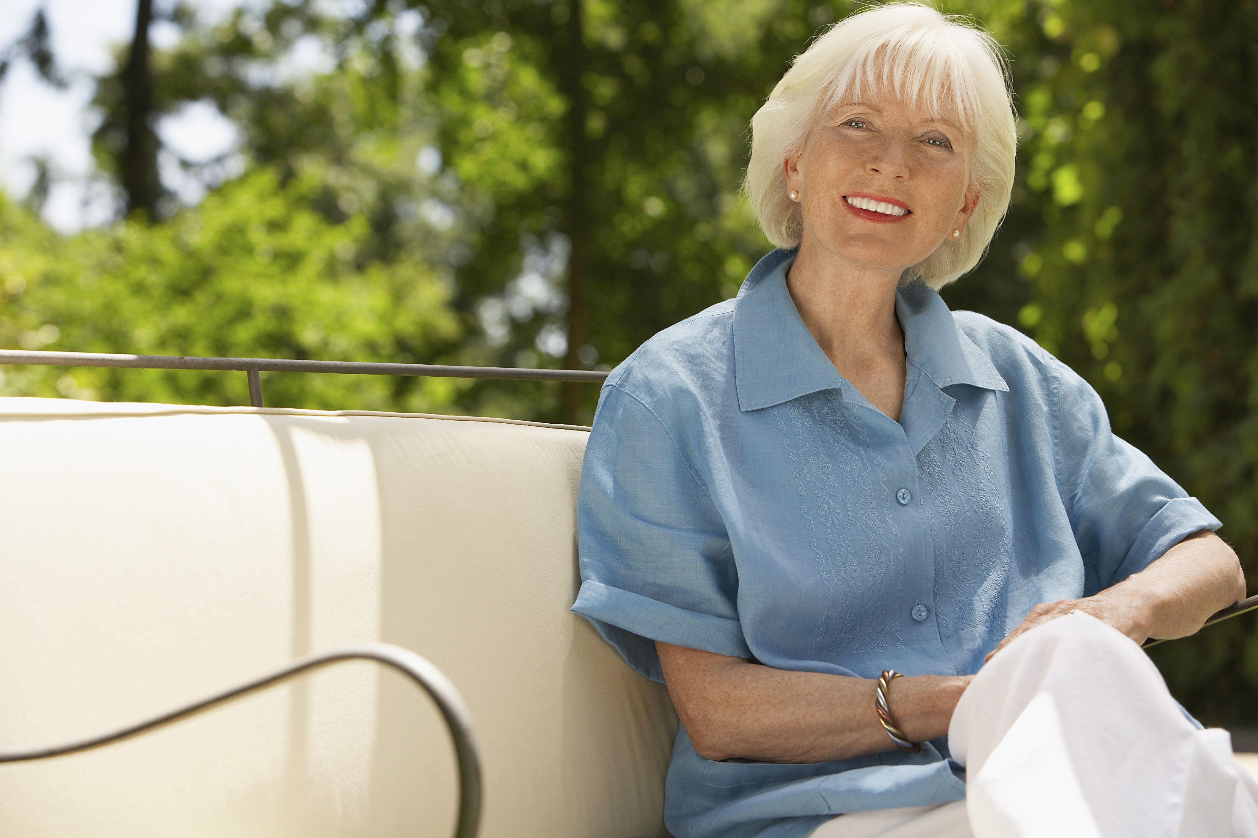 Smiling woman with short white hair sitting on lounge chair outside